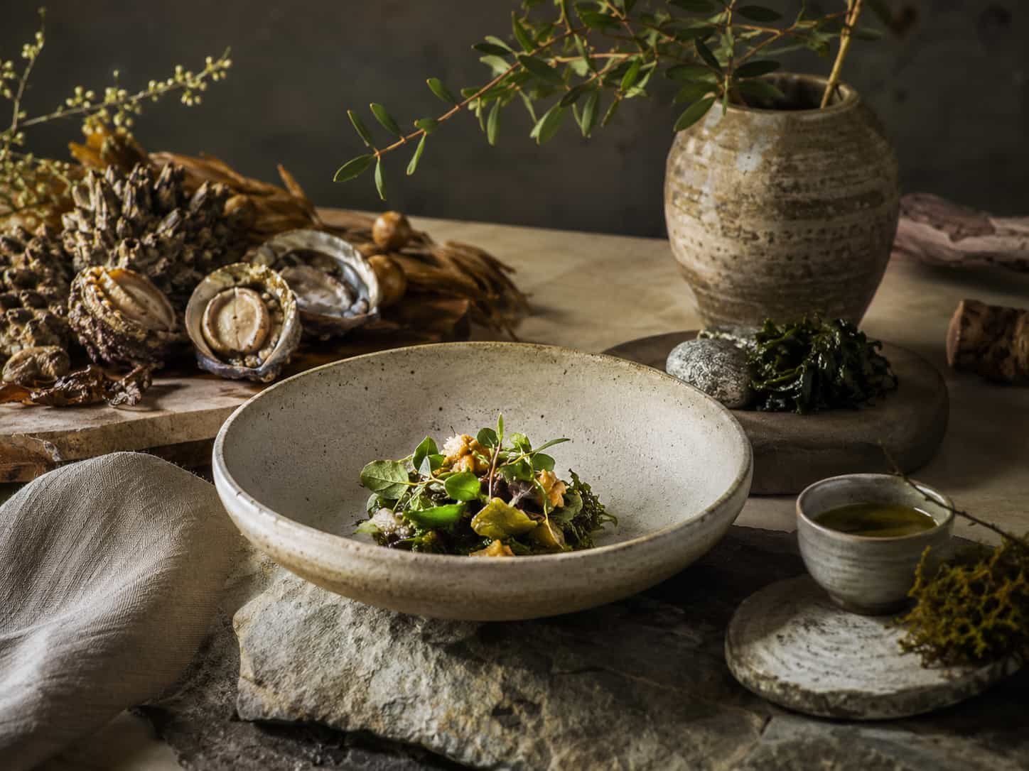 Poetisches Fine-Dining-Stillleben mit regionalen Zutaten, handwerklicher Keramik, Leinen und natürlichen Materialien.