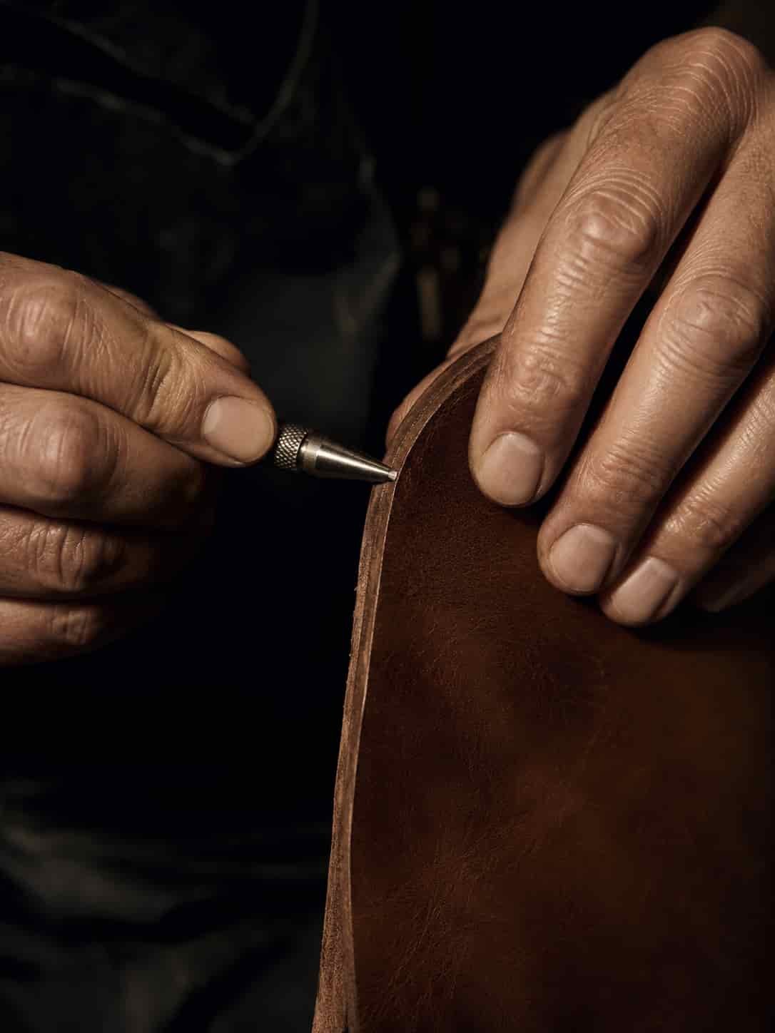 Erfahrene Handwerkerhände bei präziser Arbeit an hochwertigem Material mit ruhigem Werkbanklicht.