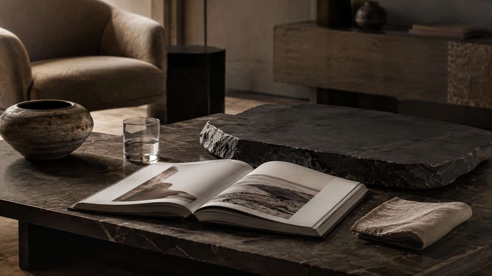 Eleganter Tisch mit Designbuch, Keramikobjekt, Glas, Leinen und ruhiger Quiet-Luxury-Atmosphäre.