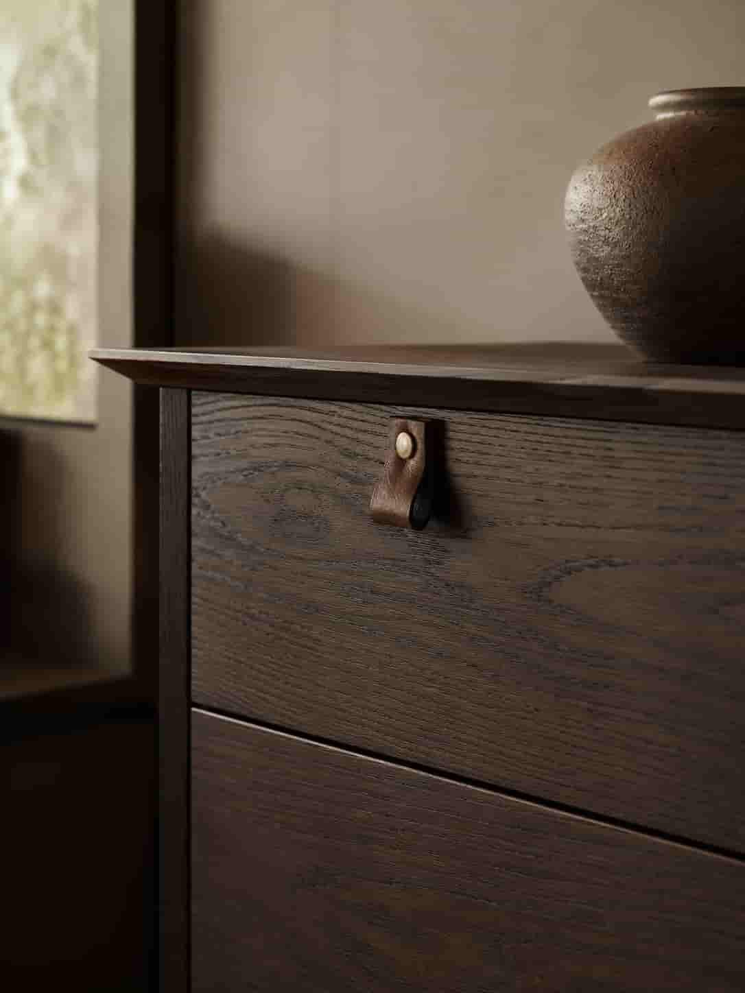 Detailaufnahme eines hochwertigen Möbelstücks aus dunklem Holz mit Maserung, feiner Kante und Messingdetail.