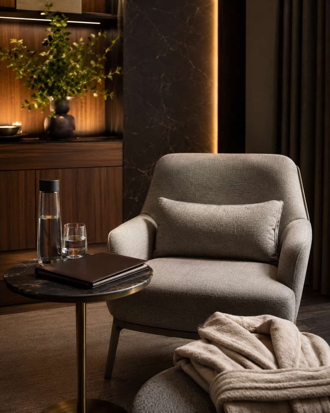 Elegante Health-Check-Lounge mit Sessel, Wasser, geschlossener Gesundheitsmappe und ruhiger Privacy-Atmosphäre.